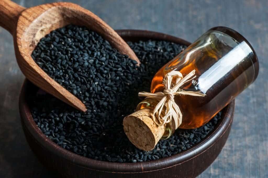 Black sesame seeds in a wooden scoop and a small glass bottle of essential oil on a dark wooden surface, representing holistic health, natural remedies, and wellness.