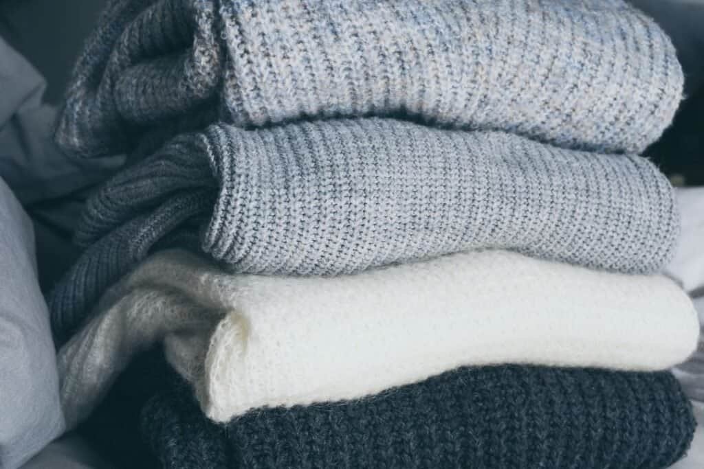 Soft, cozy folded sweaters and blankets in neutral tones, perfect for creating a warm and inviting holistic home environment. Ideal for enhancing comfort and wellness at home.