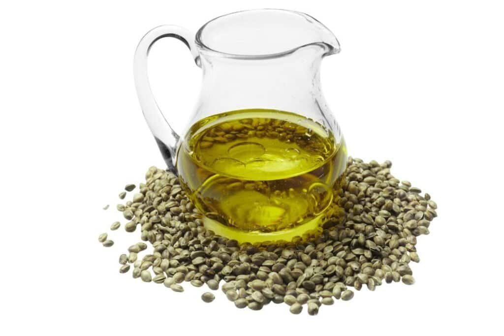 Organic hemp seed oil in a glass pitcher with hemp seeds on white background, promoting holistic health and wellness in eco-friendly home remedies.
