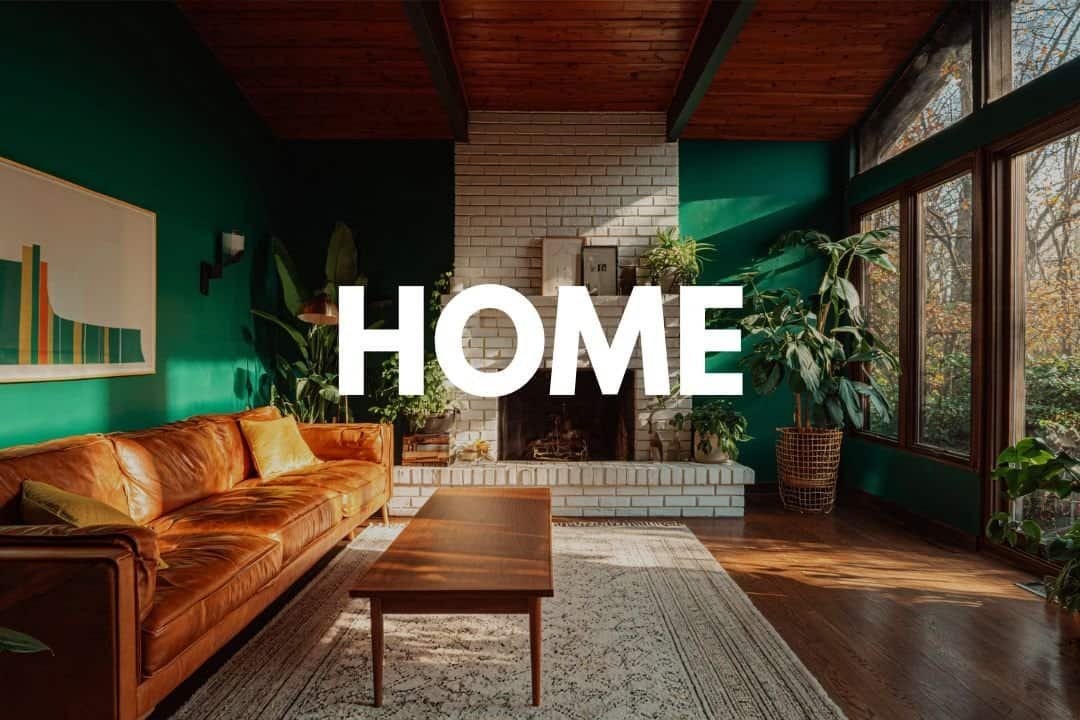 Cozy living room with modern decor, green accent wall, large windows, and indoor plants, featuring a leather sofa, white brick fireplace, wooden coffee table, and natural sunlight, perfect for holistic home design.