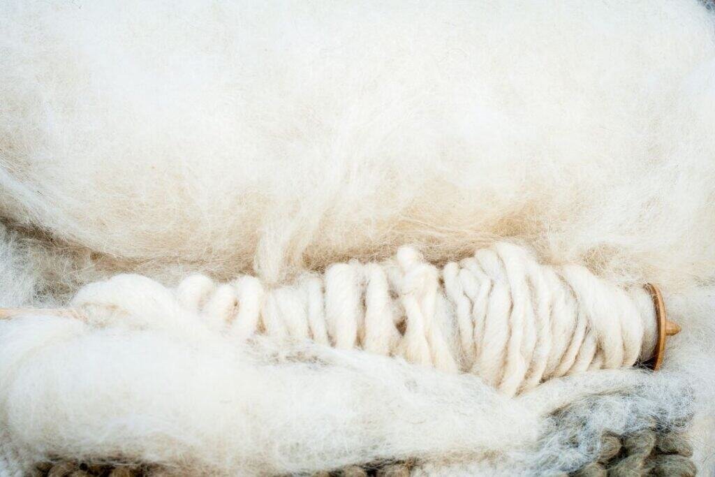 Soft white merino wool fibers on a spinning wheel, emphasizing natural wool, sustainable fibers, and eco-friendly home decor.