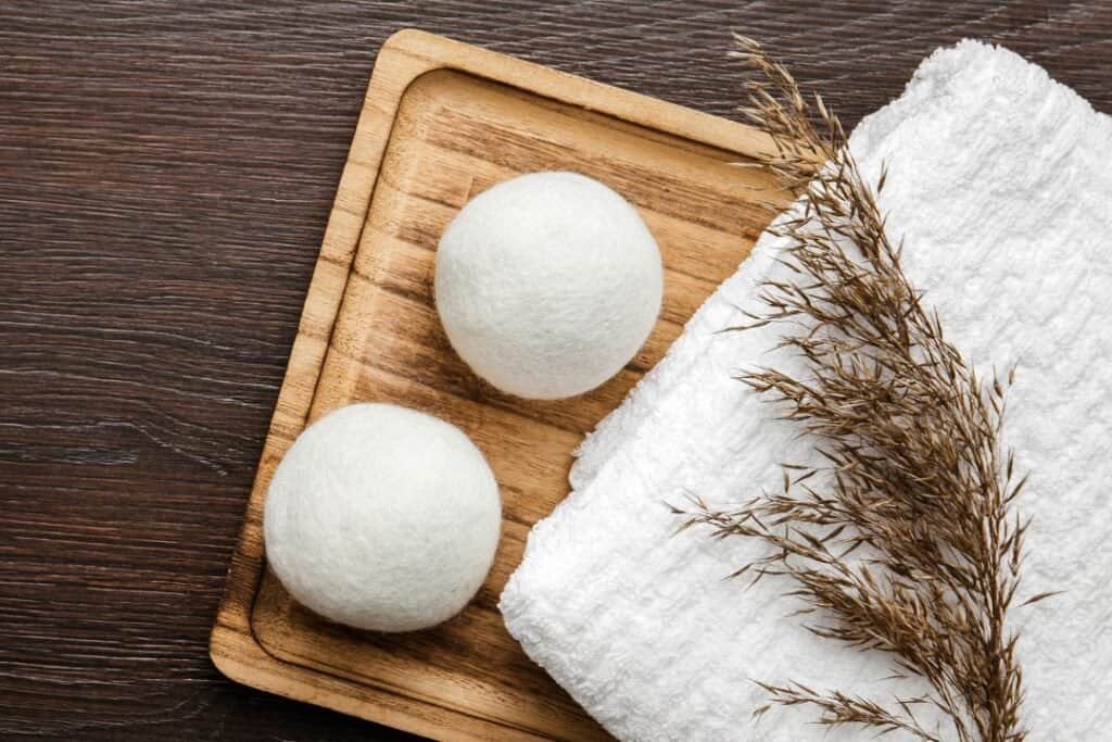 Soft white bath bombs on a wooden tray with a folded white towel and dried decorative plant for a relaxing, holistic home spa experience.