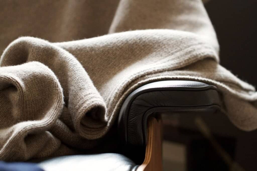 Soft beige cashmere sweater draped over a modern black leather chair, embodying cozy and minimalist home decor.