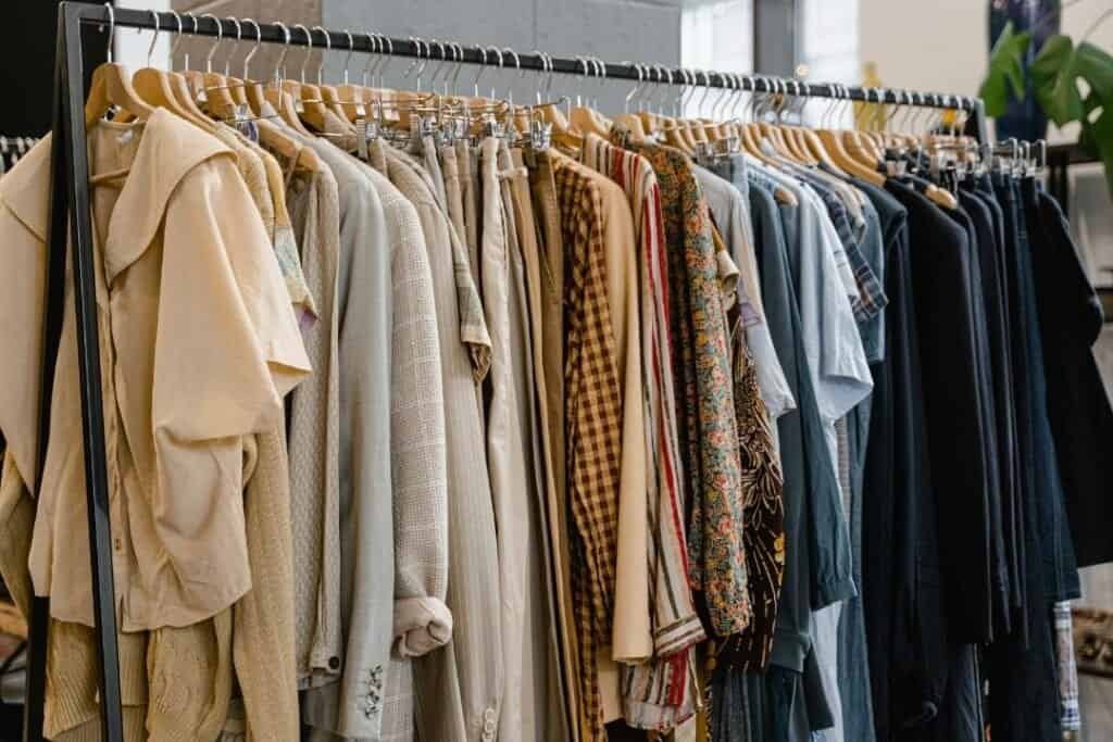 Clothing rack with beige, checkered, floral, and striped shirts and jackets in a cozy home decor store or boutique setting.