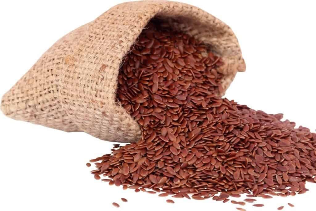 Golden flax seeds spilled from a rustic burlap sack on a white background, ideal for promoting holistic home health and wellness practices.