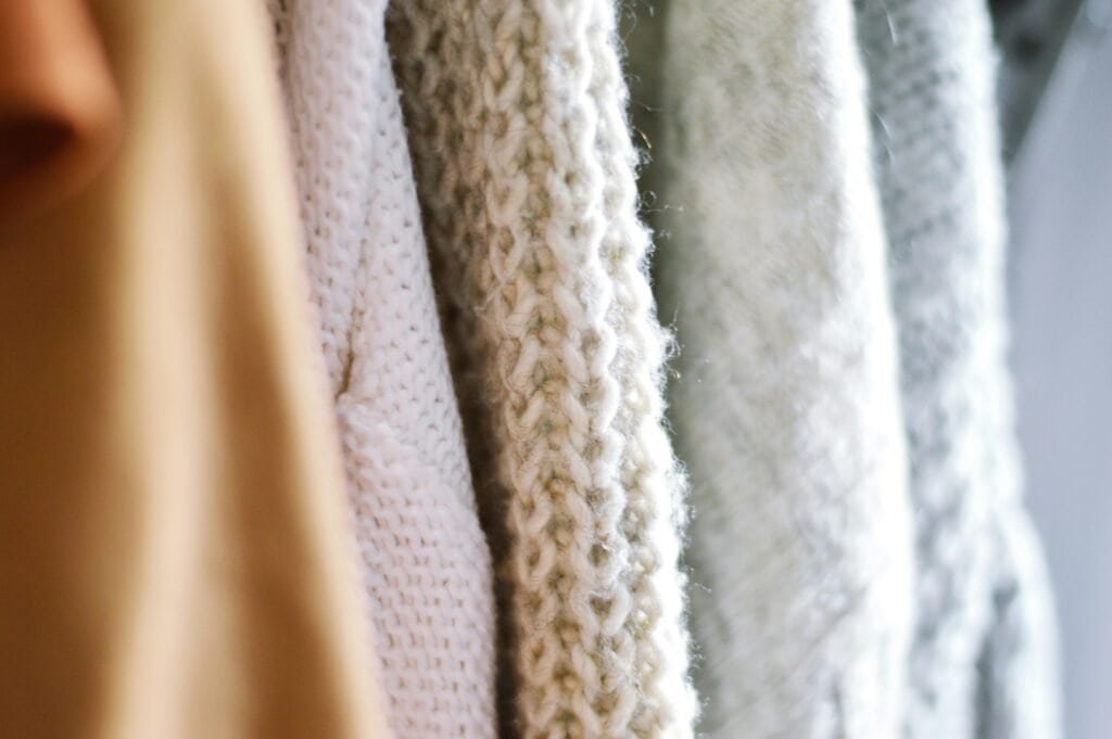 Soft, cozy knitted and merino wool sweaters hanging on a wardrobe, emphasizing sustainable and natural home decor choices.